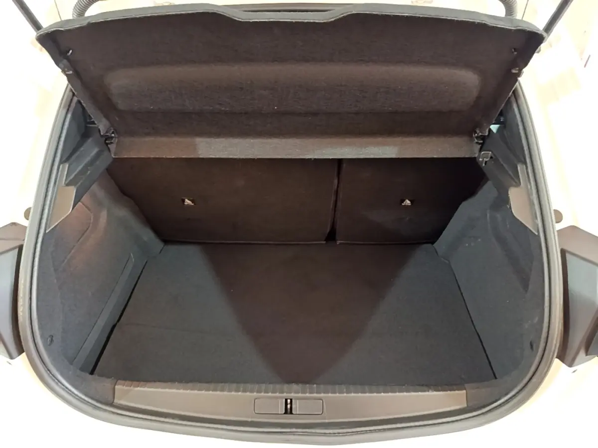 Coffre ouvert vu de l'arrière d'une Peugeot 208 blanche, montrant l'espace de chargement vide et les sièges rabattables.