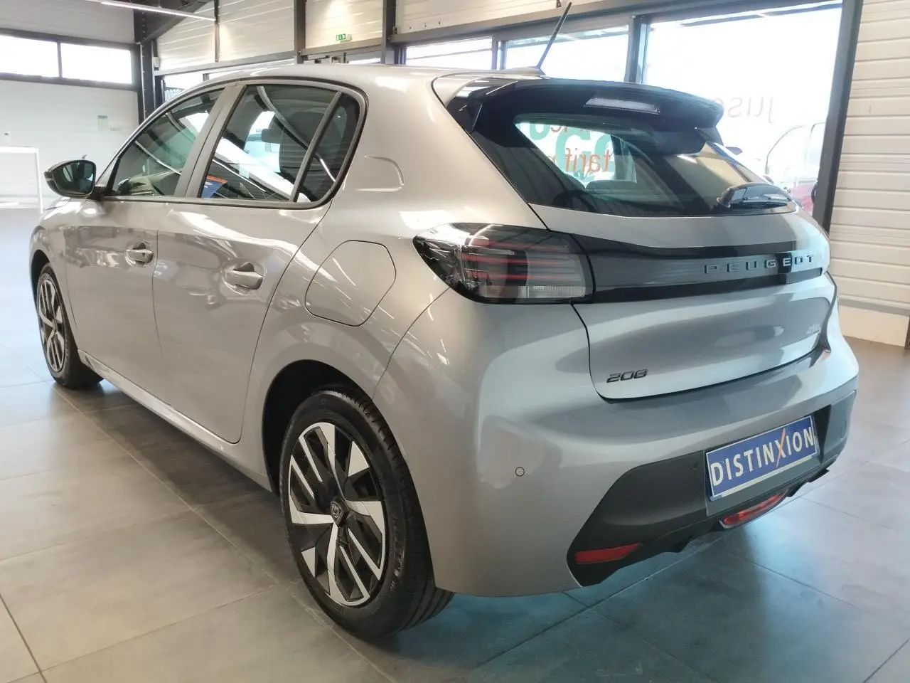 Vue 3/4 arrière droite d'une Peugeot 208 2024 gris Artense avec feux arrière noirs et jantes bicolores en concession.
