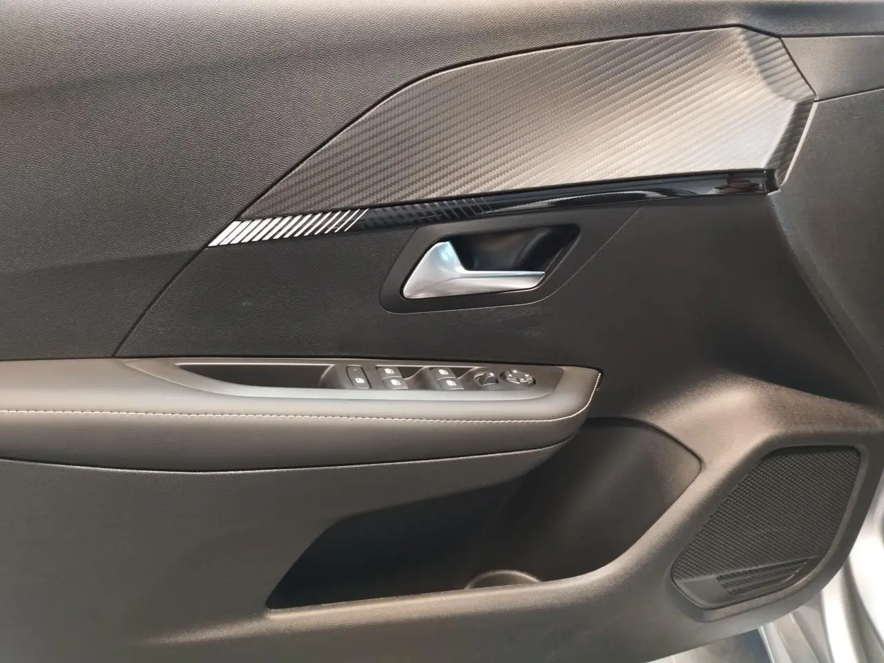 Gros plan sur la porte côté conducteur du Peugeot 208 gris Artense 2024, avec commandes de vitres et insert décoratif noir.