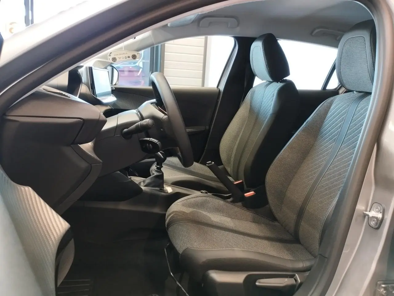 Intérieur de la Peugeot 208 2024 gris Artense, vue côté conducteur montrant les sièges et la boîte manuelle.
