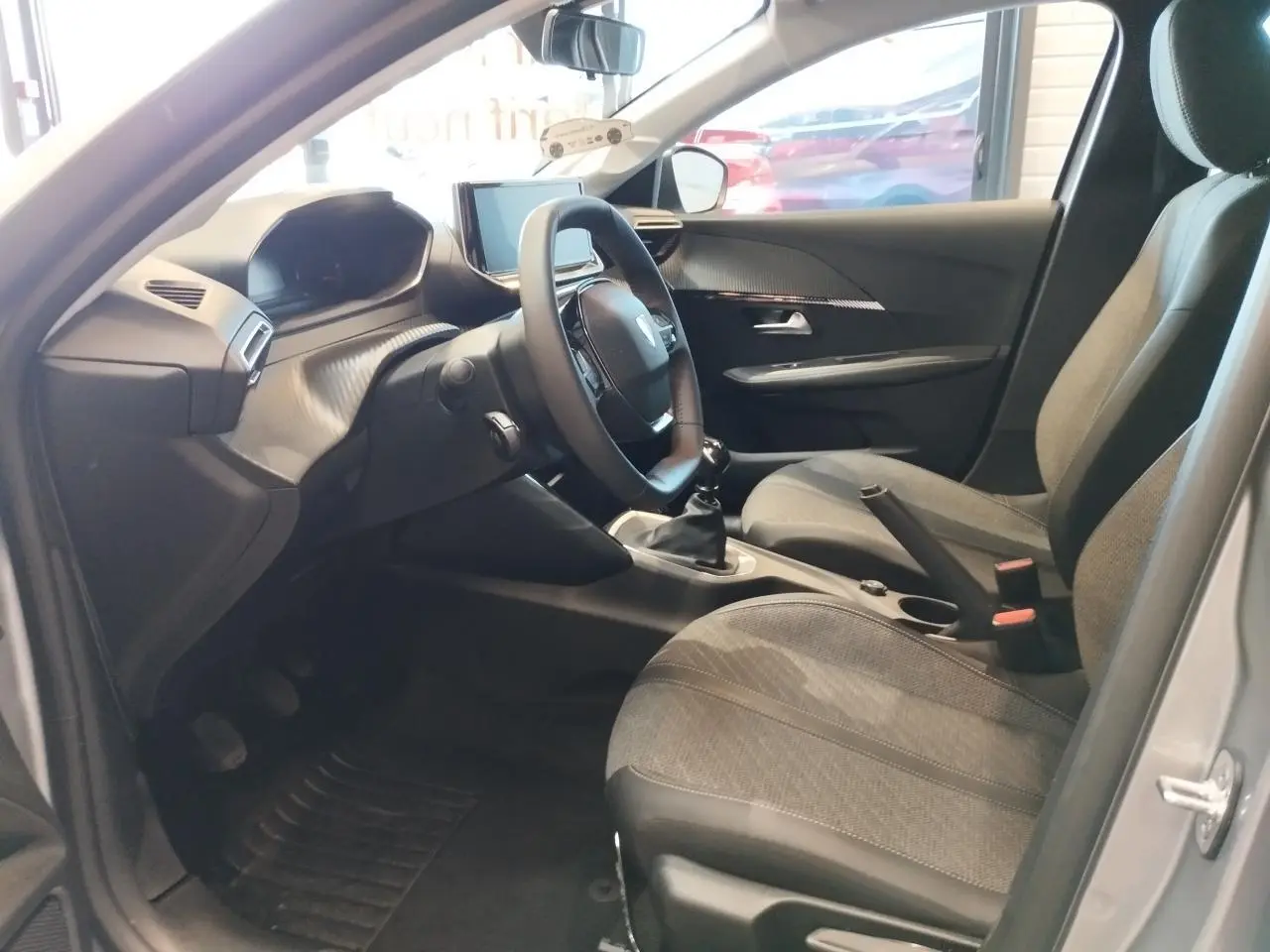 Intérieur côté conducteur de la Peugeot 208 2024 gris Artense, avec volant compact et boîte manuelle visible.