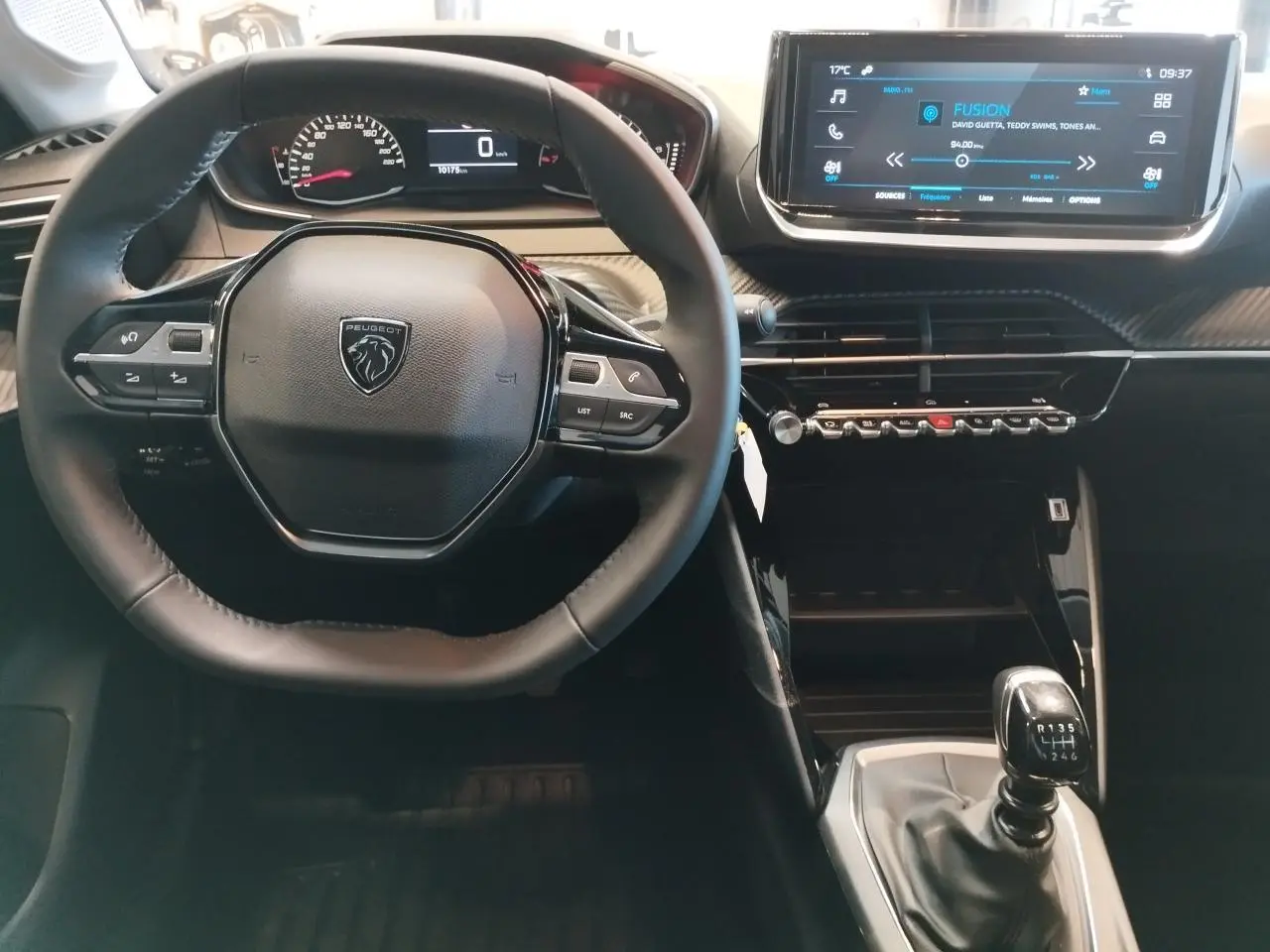 Vue intérieure centrée sur le volant Peugeot et la console centrale avec boîte manuelle dans une Peugeot 208 2024 gris Artense.