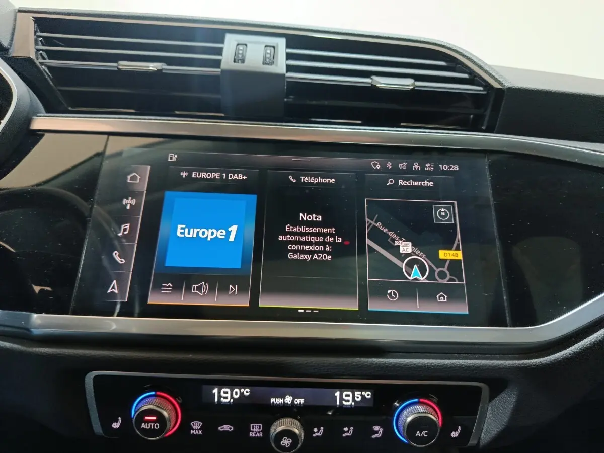 Écran tactile central de l'Audi Q3 Sportback gris foncé, affichant navigation et radio, avec commandes climatisation en dessous.