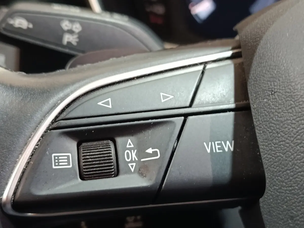 Gros plan sur les commandes multifonctions noires du volant de l'Audi Q3 Sportback hybride rechargeable, détails des boutons et molette.