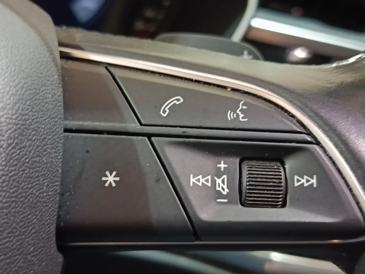 Gros plan sur les commandes vocales et volume au volant cuir noir de l'Audi Q3 Sportback gris foncé, version hybride rechargeable.