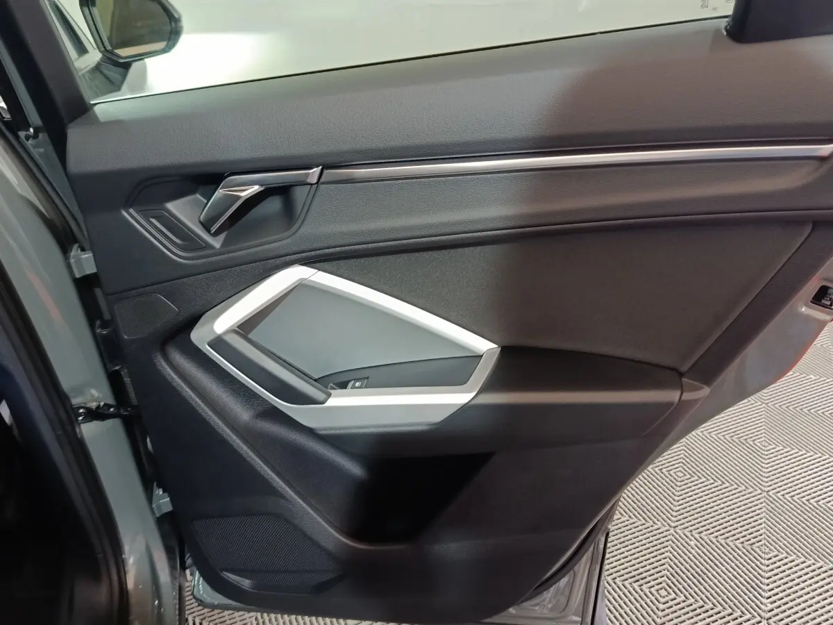 Vue intérieure de la porte avant gauche gris foncé de l'Audi Q3 Sportback 45 TFSI e avec poignée argentée et commandes vitres.