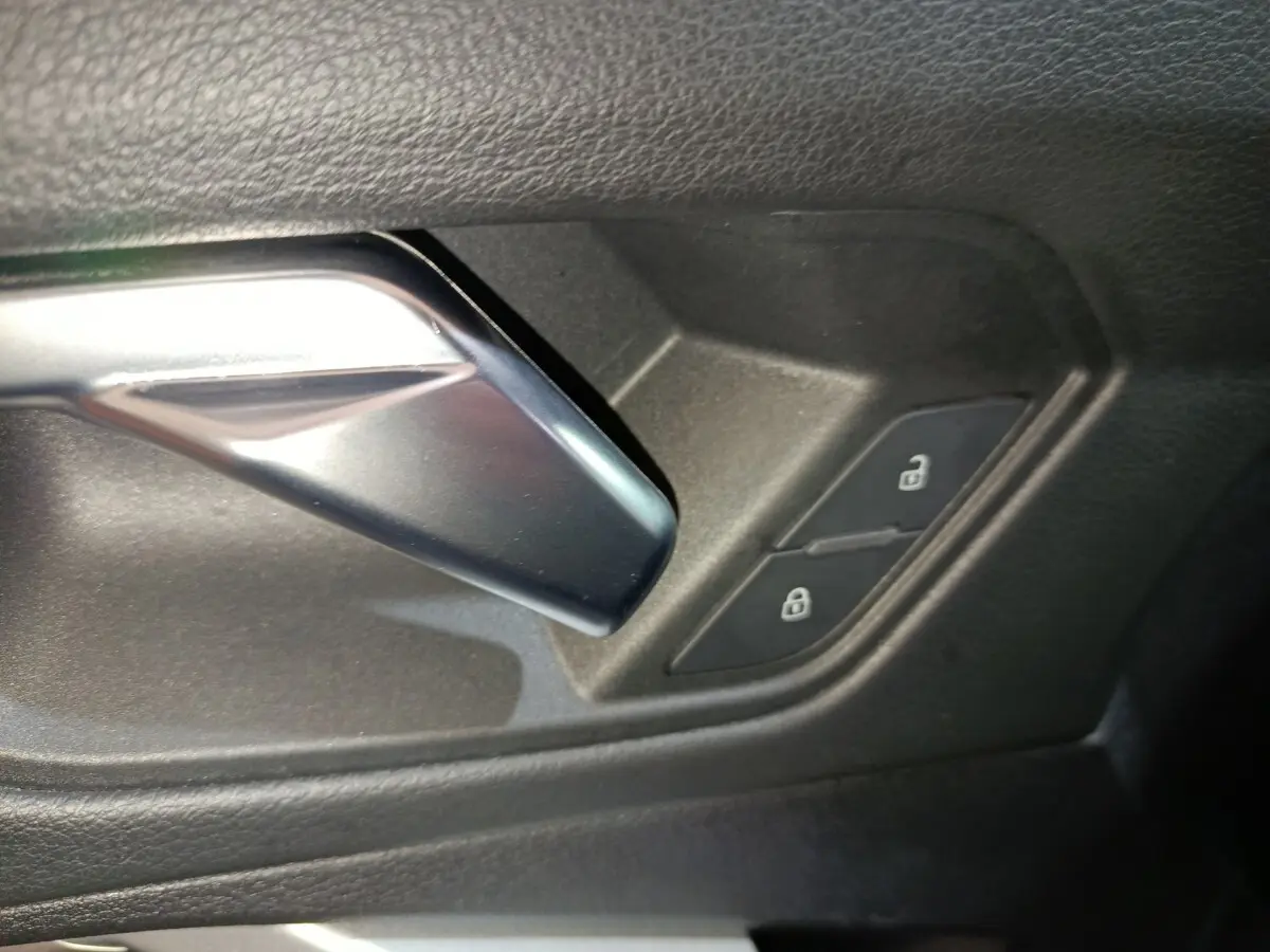 Gros plan sur la poignée intérieure argentée et les boutons de verrouillage sur la portière noire de l'Audi Q3 Sportback.