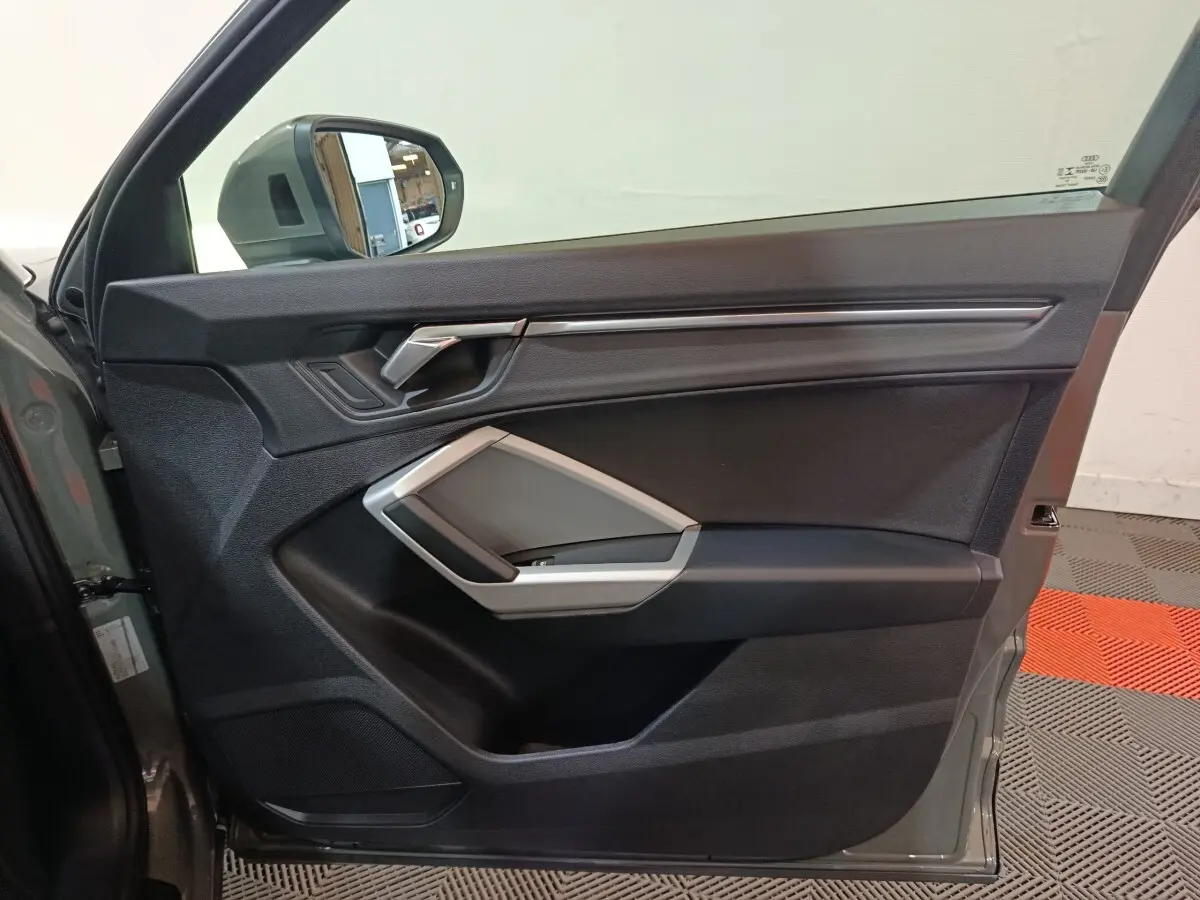 Intérieur côté gauche de la porte avant d’un Audi Q3 Sportback gris foncé, avec poignée argentée et miroir latéral visible.