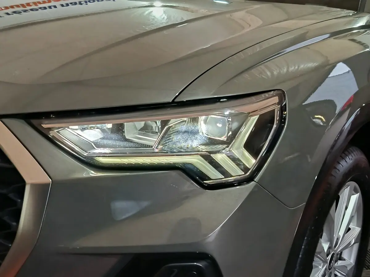 Gros plan sur le phare avant droit gris foncé de l'Audi Q3 Sportback 45 TFSI e avec jante visible.