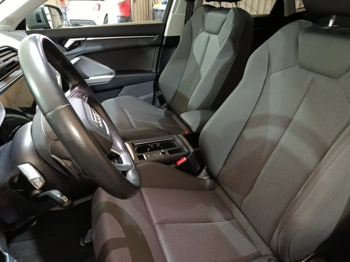 Vue intérieure côté conducteur de l'Audi Q3 Sportback gris foncé, montrant sièges tissu et volant cuir multifonctions.