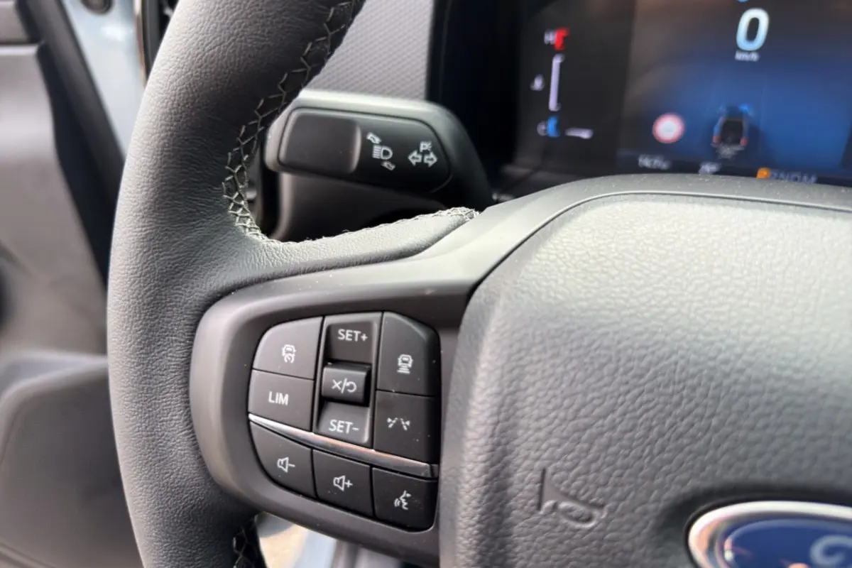Gros plan sur les commandes multifonctions du volant cuir du Ford Ranger gris commandeur, tableau de bord numérique en arrière-plan.