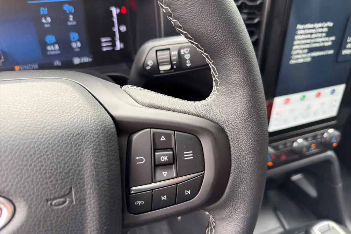 Gros plan sur le volant cuir multifonctions du Ford Ranger gris commandeur, avec écran tactile et commandes au volant visibles.