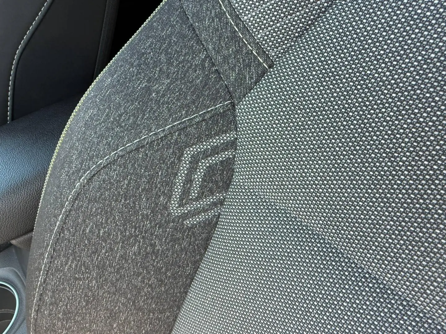 Gros plan sur le siège avant gris foncé du Renault Captur 1.6 E-Tech avec logo brodé et accoudoir en cuir noir.