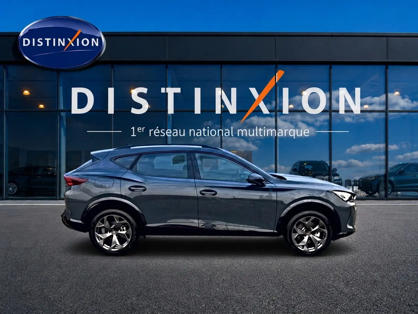 Vue latérale gauche du CUPRA Formentor 1.5 etsi hybrid 150 DSG7 en bleu fjord avec jantes 18 pouces devant un showroom Distinxion.