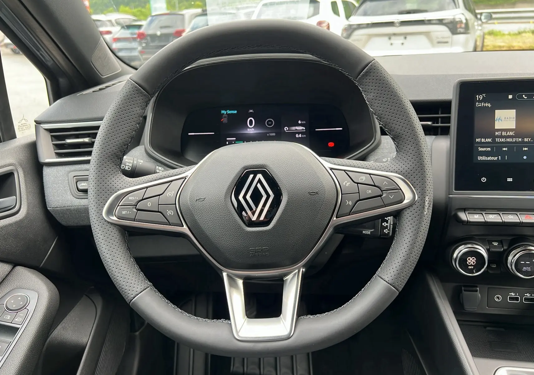 Vue rapprochée du volant perforé d'une Renault Clio V TCE 90 Techno 2025, avec tableau de bord numérique allumé.