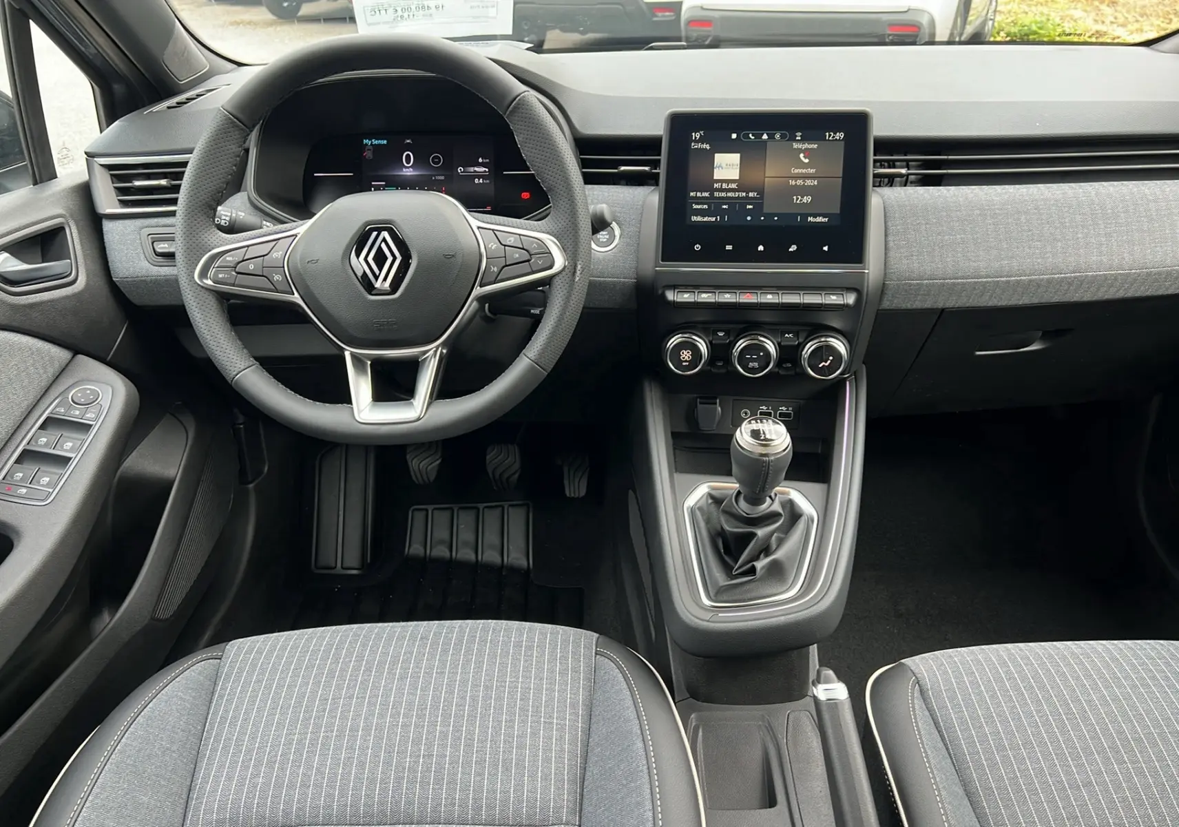 Vue intérieure avant de la Renault Clio V TCE 90 Techno 2025 avec volant multifonction et levier de vitesse manuel.