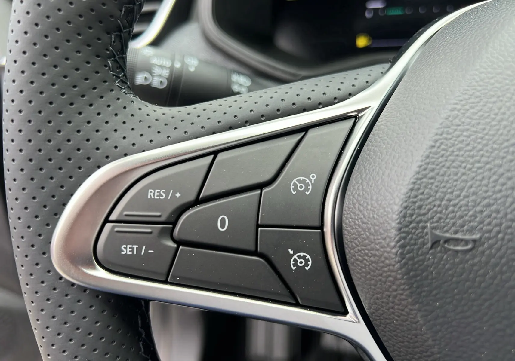 Gros plan sur les commandes de régulateur de vitesse au volant perforé d'une Renault Clio V TCe 90 Techno gris schiste 2025.