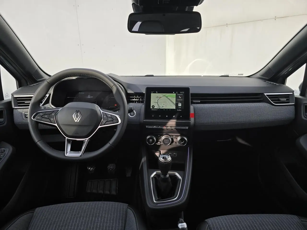 Vue intérieure avant de la Renault Clio V 2025 gris Rafale Métal avec tableau de bord moderne et boîte manuelle.