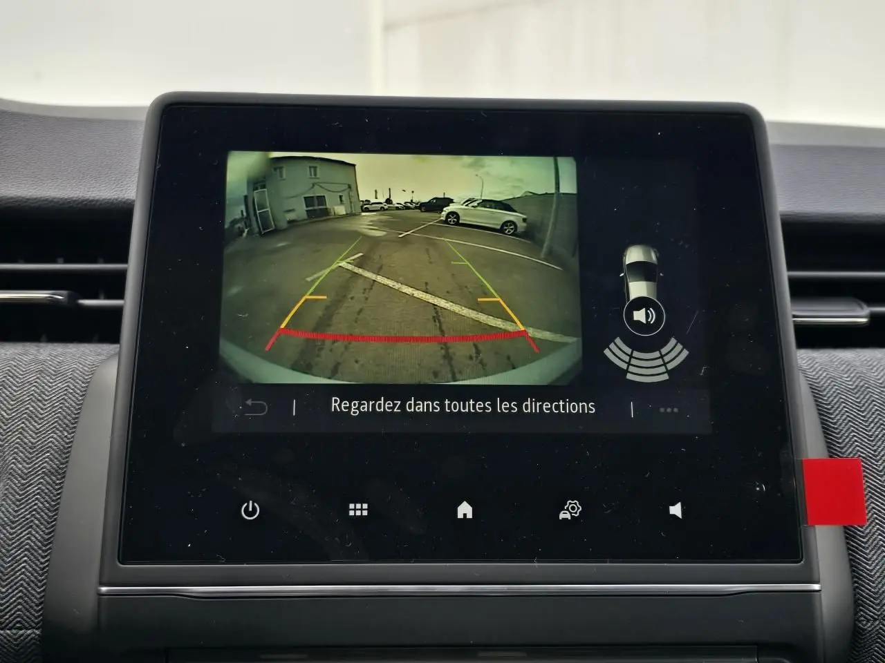 Écran multimédia affichant la caméra de recul d'une Renault Clio gris Rafale, vue arrière avec lignes de guidage colorées.