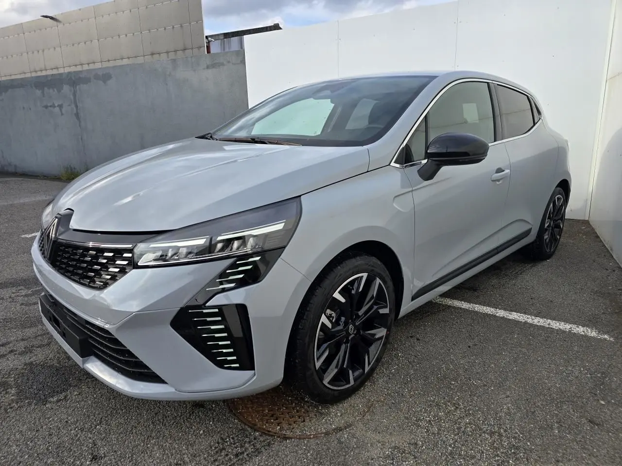 Renault Clio 2025 gris Rafale métal vue 3/4 avant droit, jantes alliage noires et détails chromés visibles.