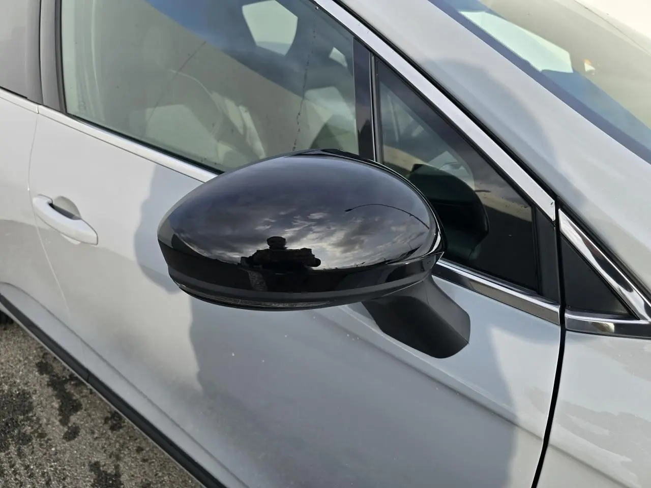 Rétroviseur noir brillant côté gauche d'une Renault Clio V gris Rafale métal, avec contour de vitres chromé visible.