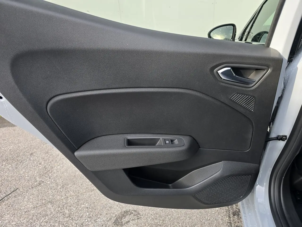 Gros plan sur la porte avant gauche intérieure noire d'une Renault Clio 2025, avec poignée argentée et commande de vitre.