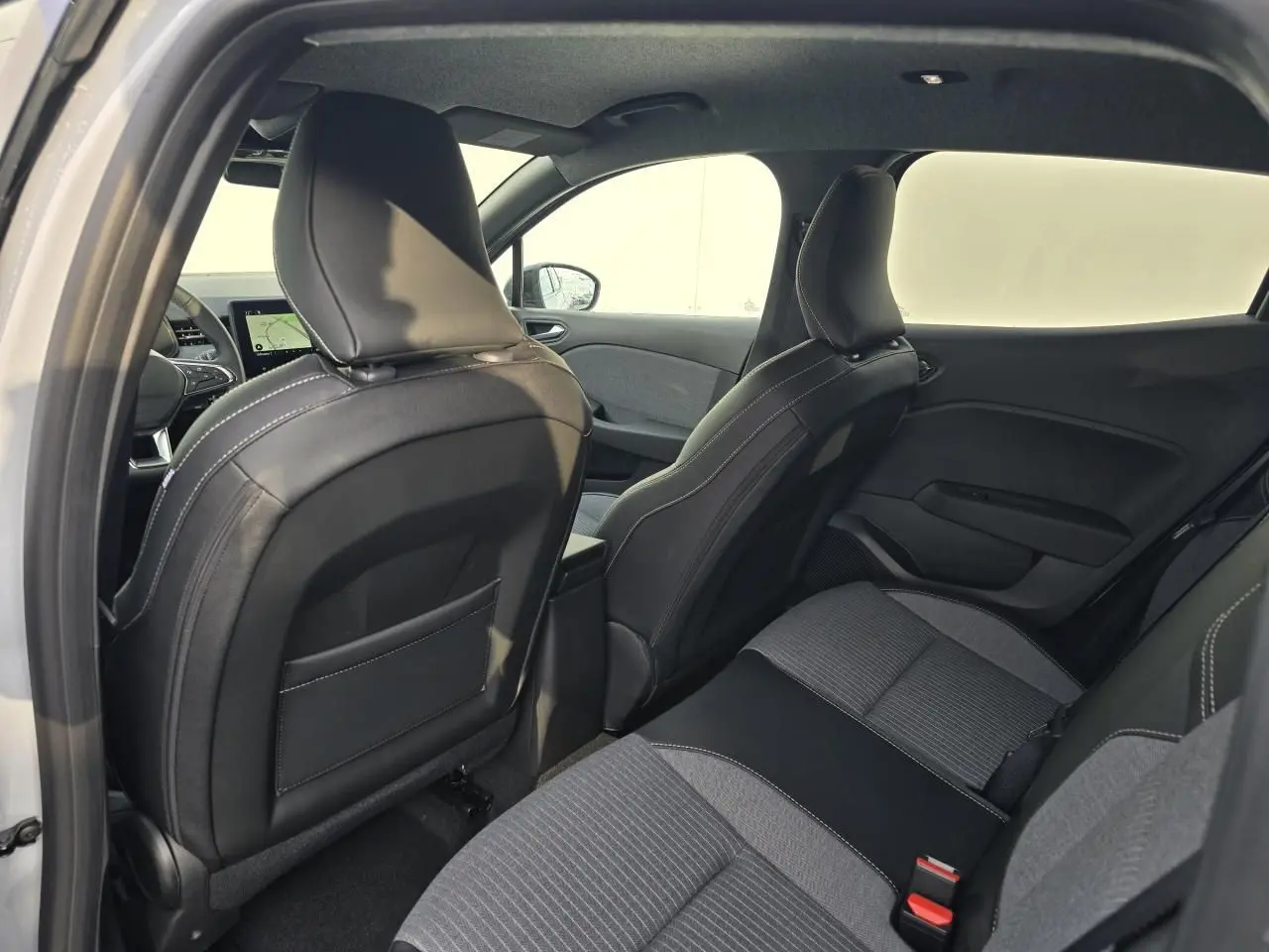 Vue intérieure arrière droite de la Renault Clio 2025, sièges tissu gris mélangé avec surpiqûres blanches et accoudoir central.