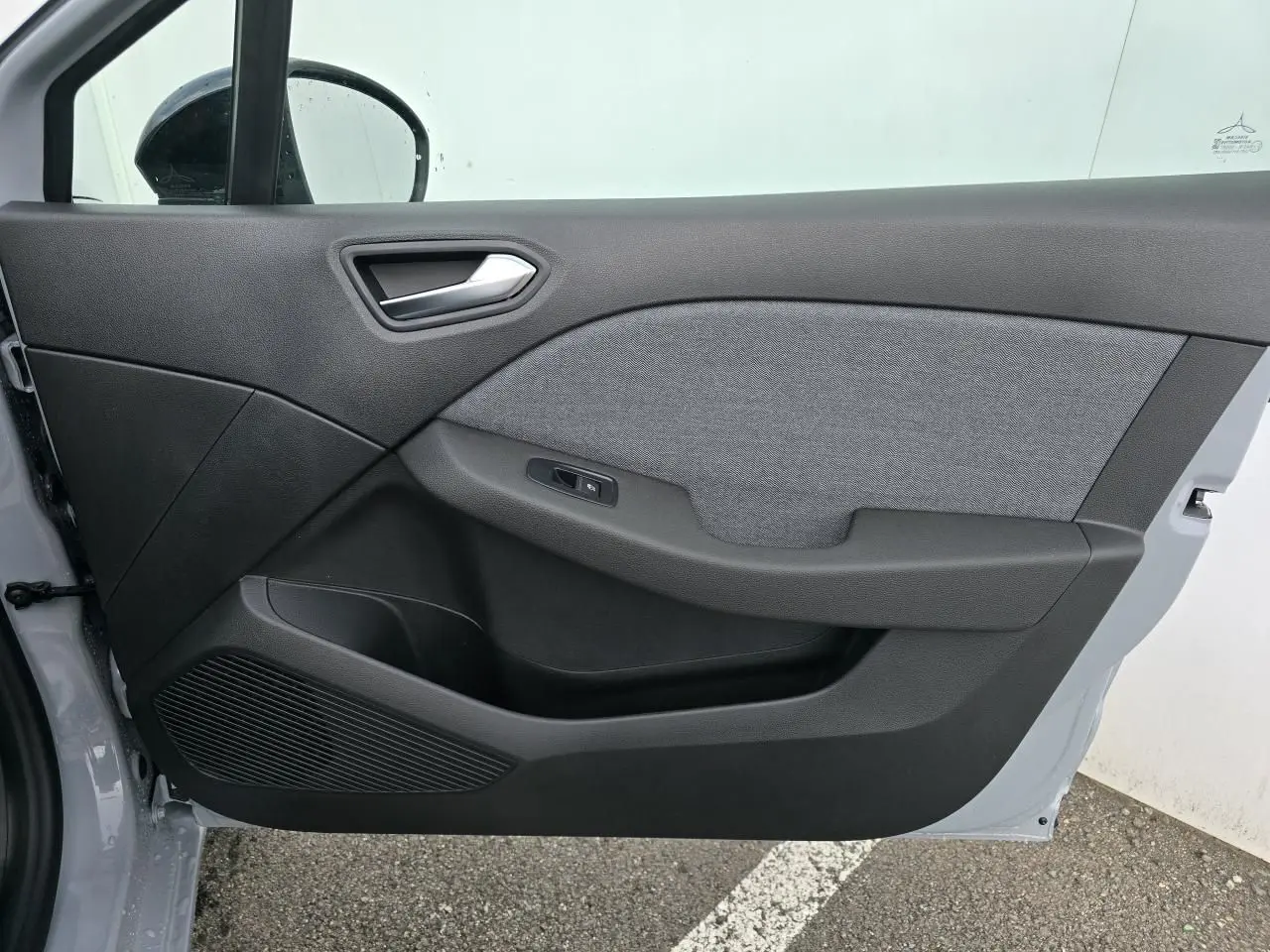 Vue intérieure de la porte avant gauche de la Renault Clio 2025 gris Rafale avec habillage tissu gris et plastique noir.