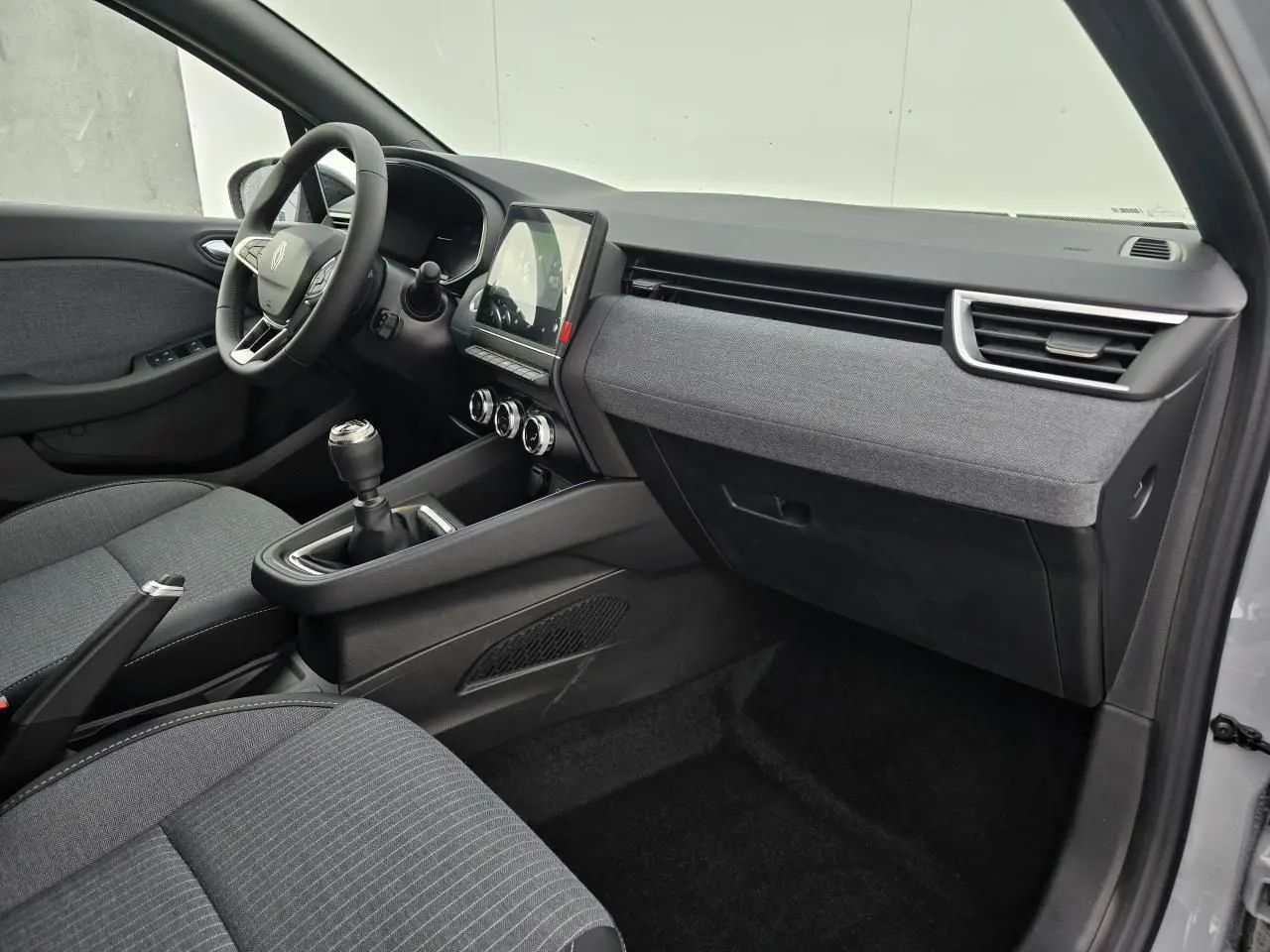 Intérieur avant droit de la Renault Clio V 2025 gris Rafale, avec tableau de bord tissu gris et boîte manuelle.