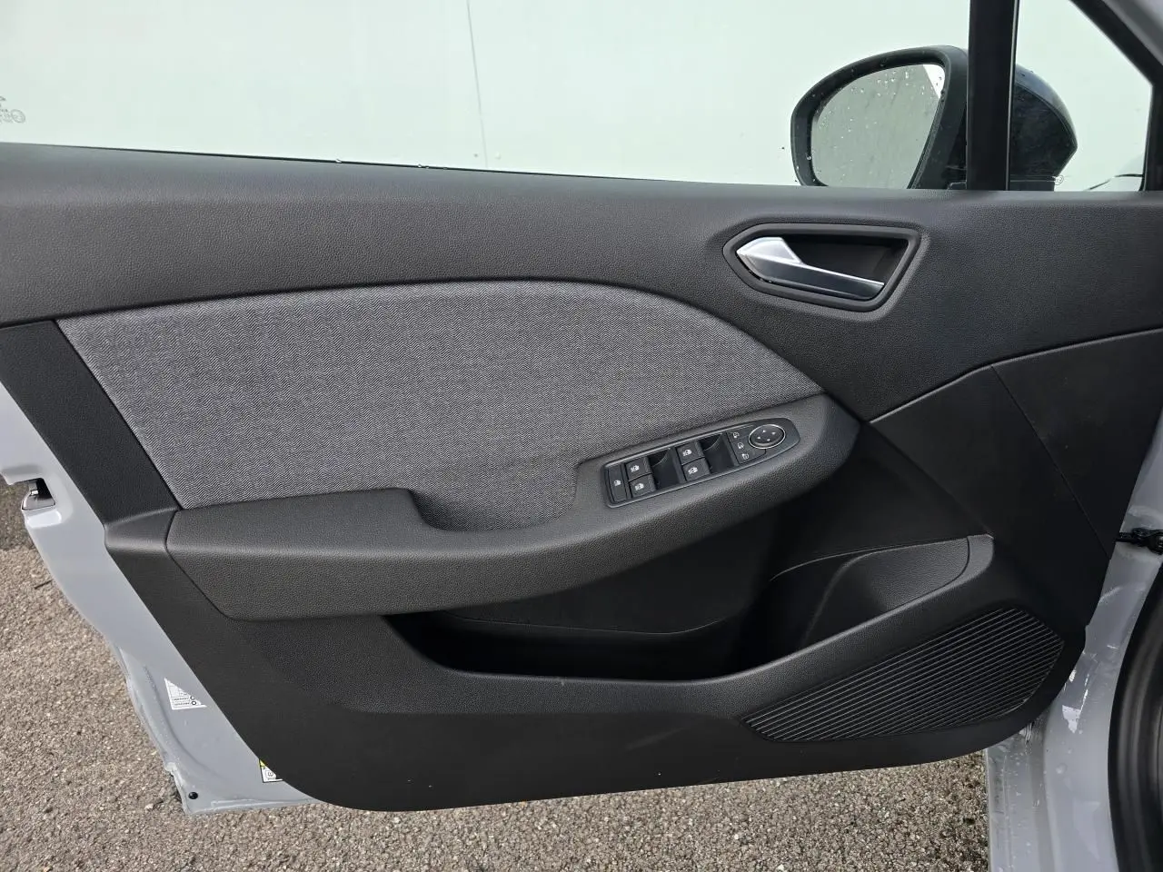 Vue intérieure de la porte avant gauche de la Renault Clio gris Rafale, avec commandes de vitres et poignée argentée.