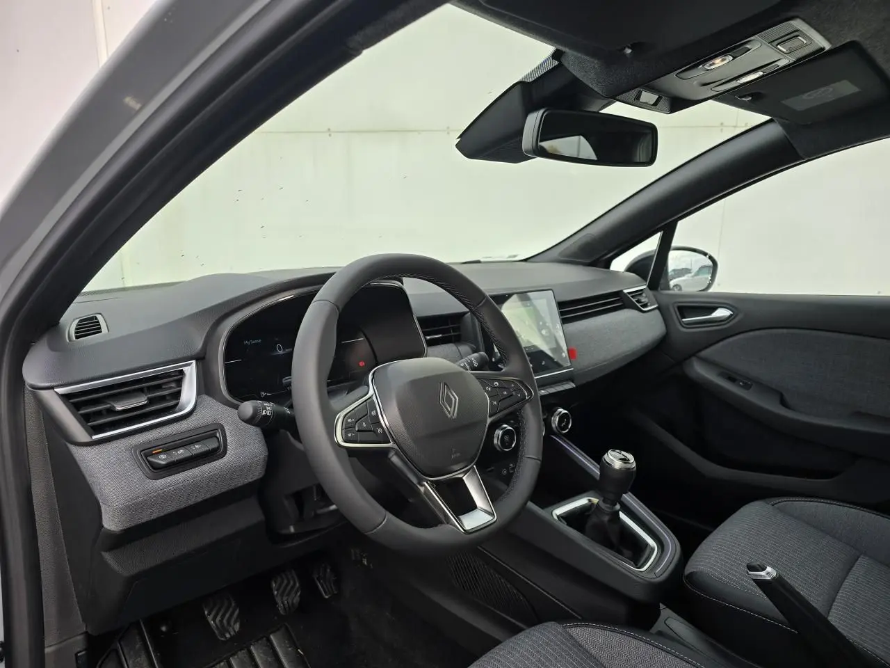 Intérieur avant droit de la Renault Clio V 2025 avec tableau de bord gris mélangé et boîte manuelle.