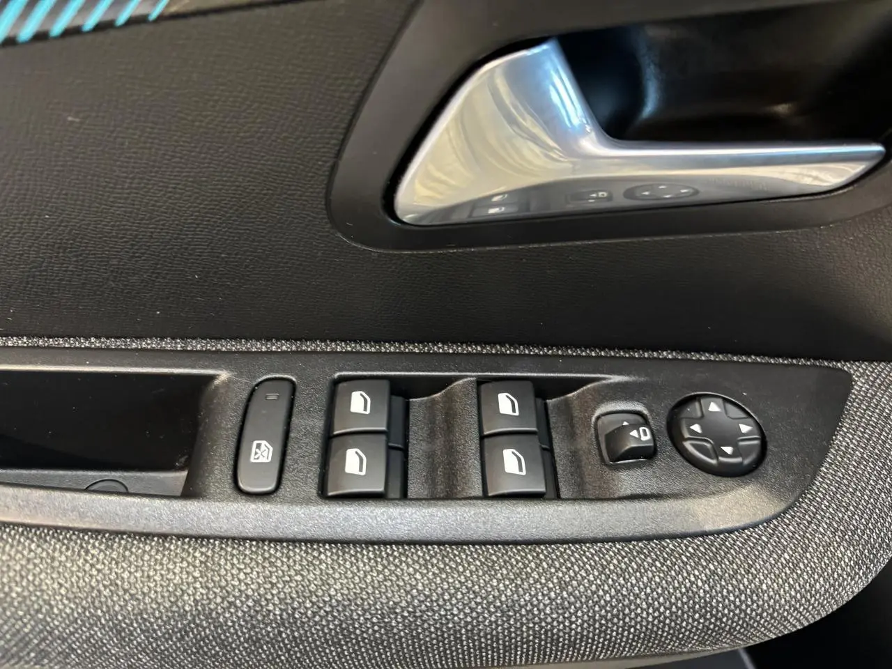 Détail des commandes de lève-vitres et réglage des rétroviseurs sur la porte intérieure côté gauche d'une Peugeot 208 blanche.
