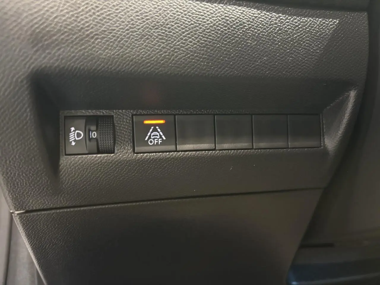 Gros plan sur les commandes noires du tableau de bord gauche d'une Peugeot 208 blanche, avec témoin d'alerte activé.