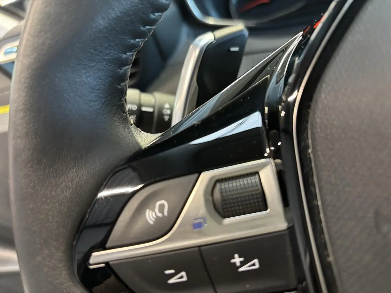 Gros plan sur les commandes noires et chrome du volant cuir de la Peugeot 208 blanche, côté gauche.