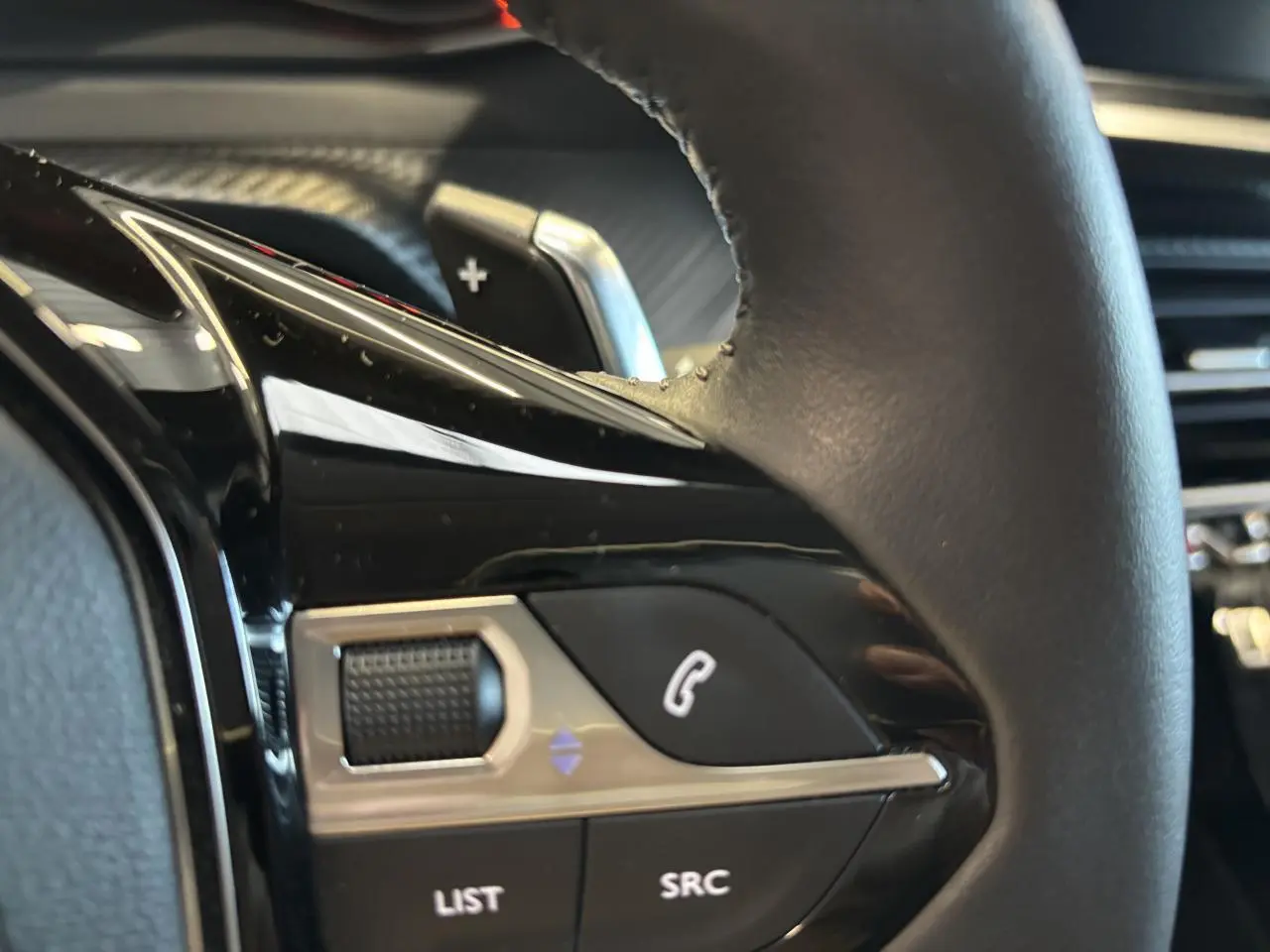 Gros plan sur commandes multimédia noires et chrome sur le volant cuir de la Peugeot 208 blanche, côté gauche.