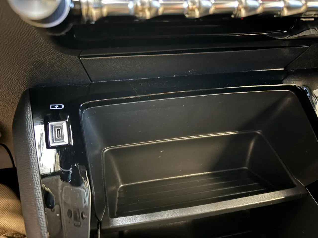 Gros plan sur la console centrale noire de la Peugeot 208 blanche, avec prise USB visible à gauche.