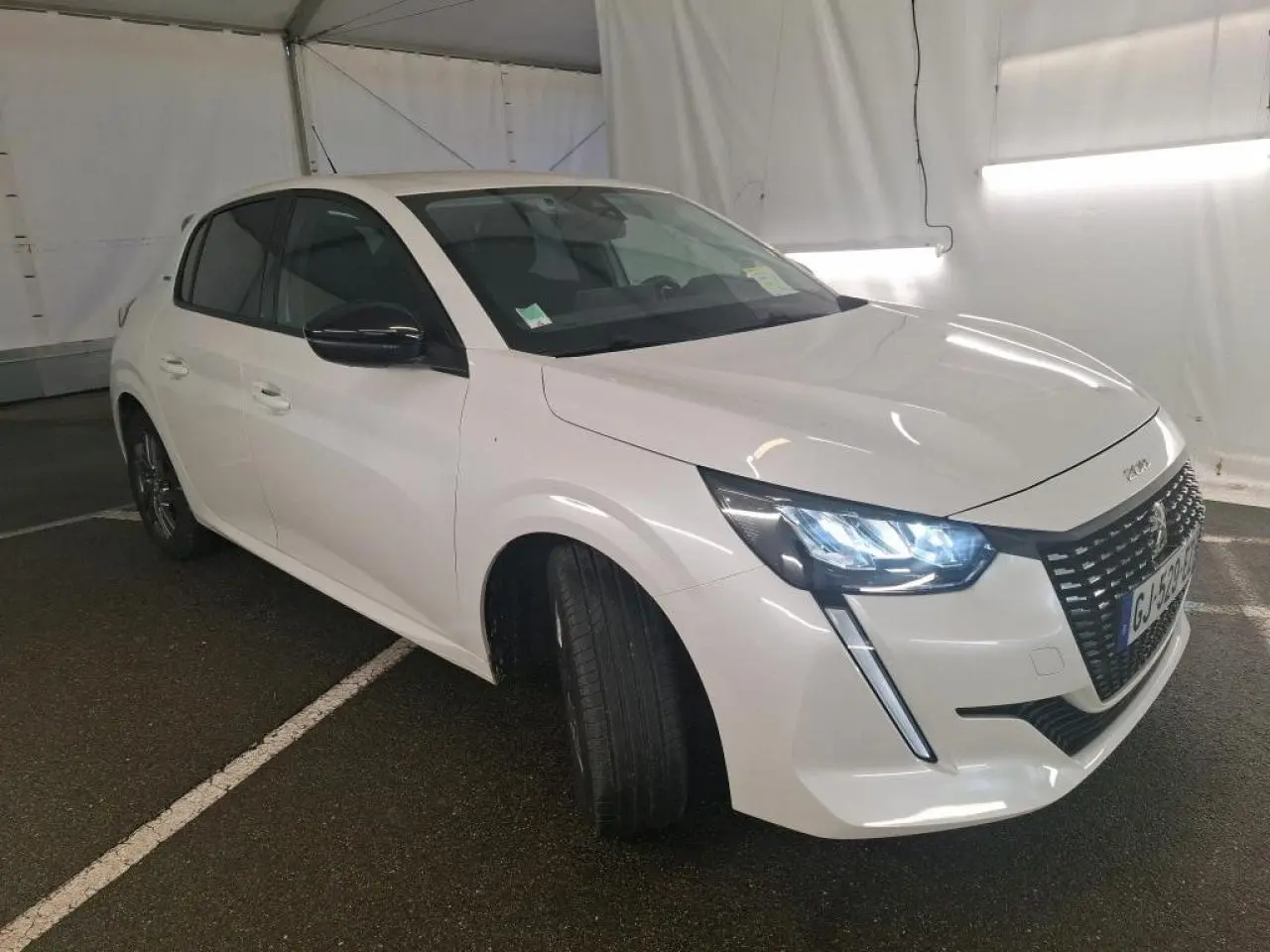 Peugeot 208 blanche vue 3/4 avant droit avec phares LED allumés et calandre noire brillante.