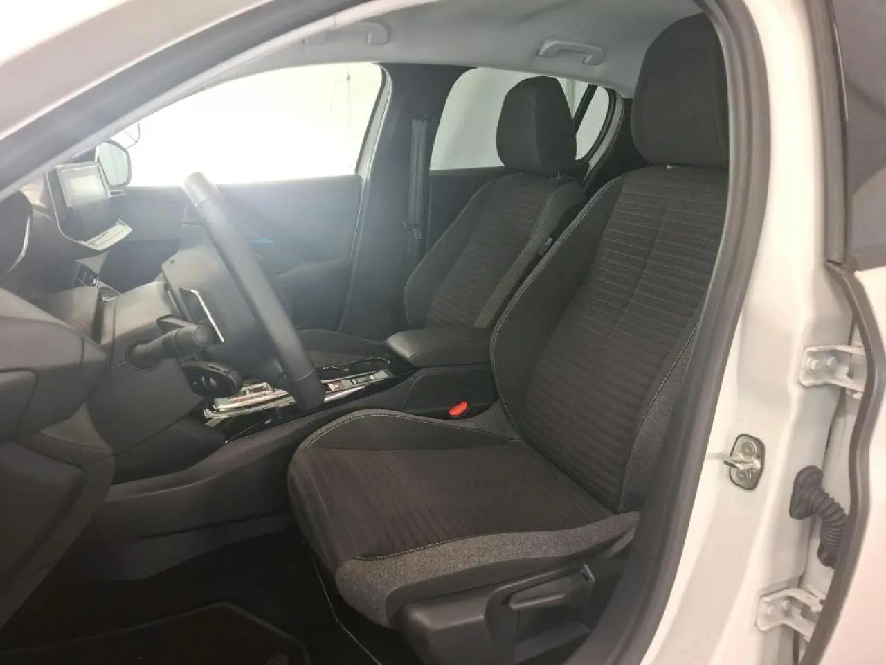 Vue intérieure côté conducteur de la Peugeot 208 blanche, sièges tissu noir avec surpiqûres bleu Azure et console centrale.