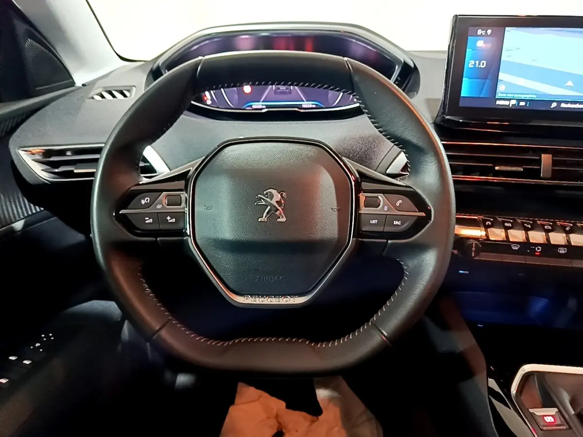 Vue intérieure centrée sur le volant cuir noir du Peugeot 5008 avec tableau de bord digital et écran tactile à droite.