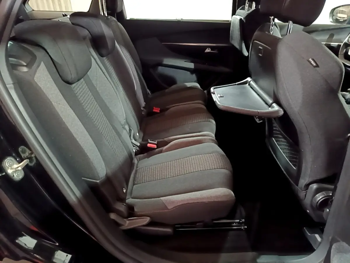 Vue intérieure côté gauche des sièges arrière noirs du Peugeot 5008 avec tablette rabattable sur le dossier avant.