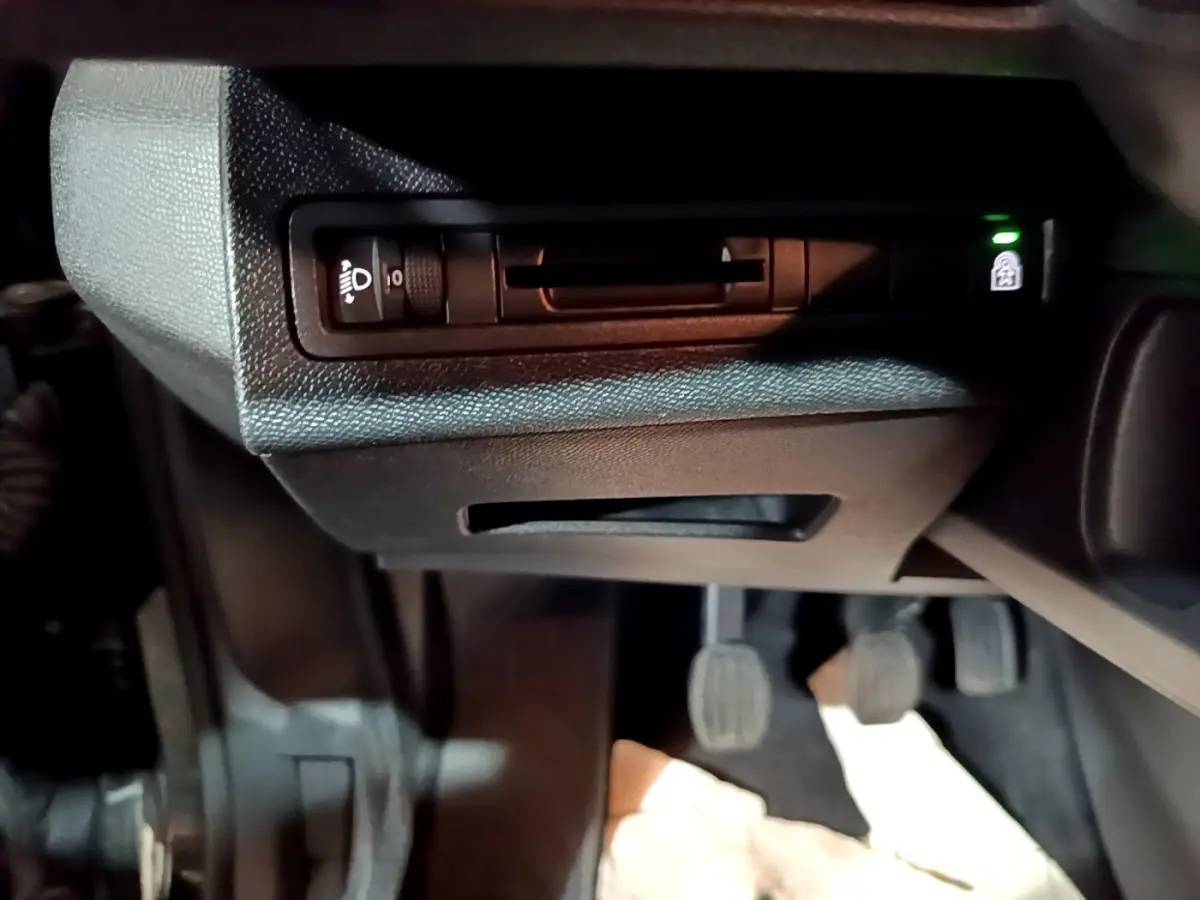 Détail intérieur du tableau de bord côté gauche avec commande de réglage des phares et pédales visibles.