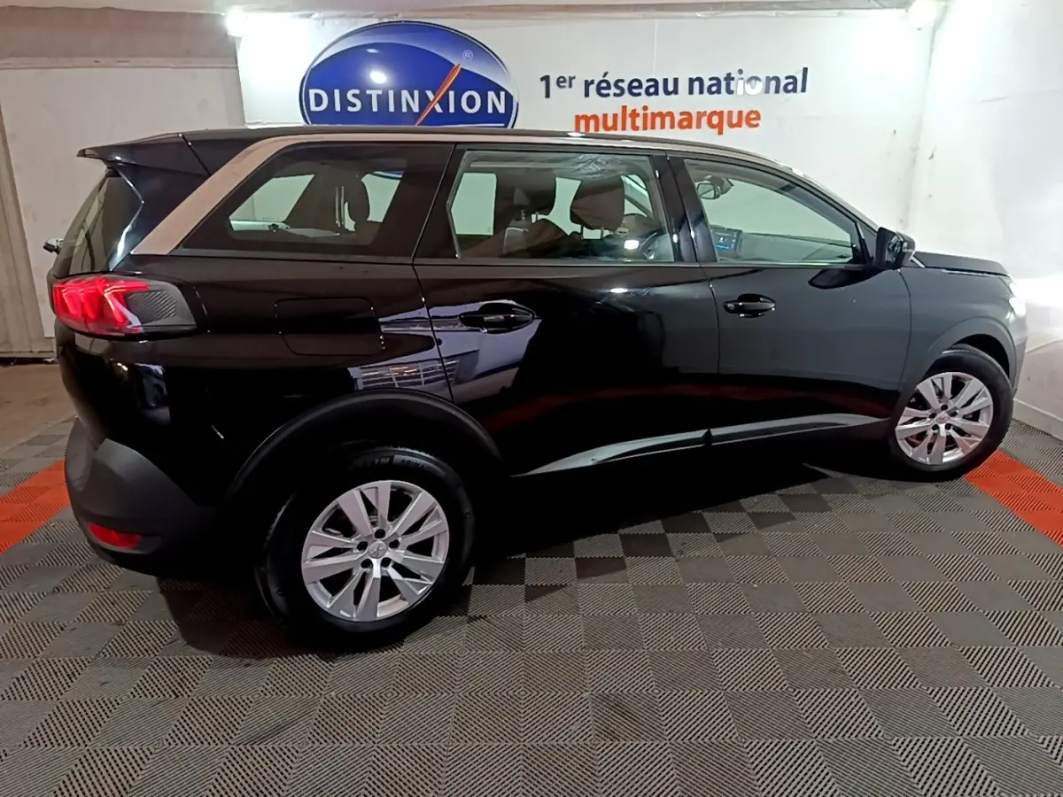 Peugeot 5008 noir vue de profil côté droit en intérieur avec jantes alliage et feux arrière LED allumés.