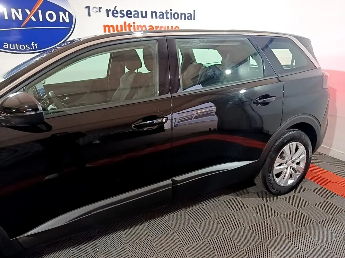 Profil côté gauche d’un Peugeot 5008 noir 2021, montrant les portes arrière et avant dans un showroom.