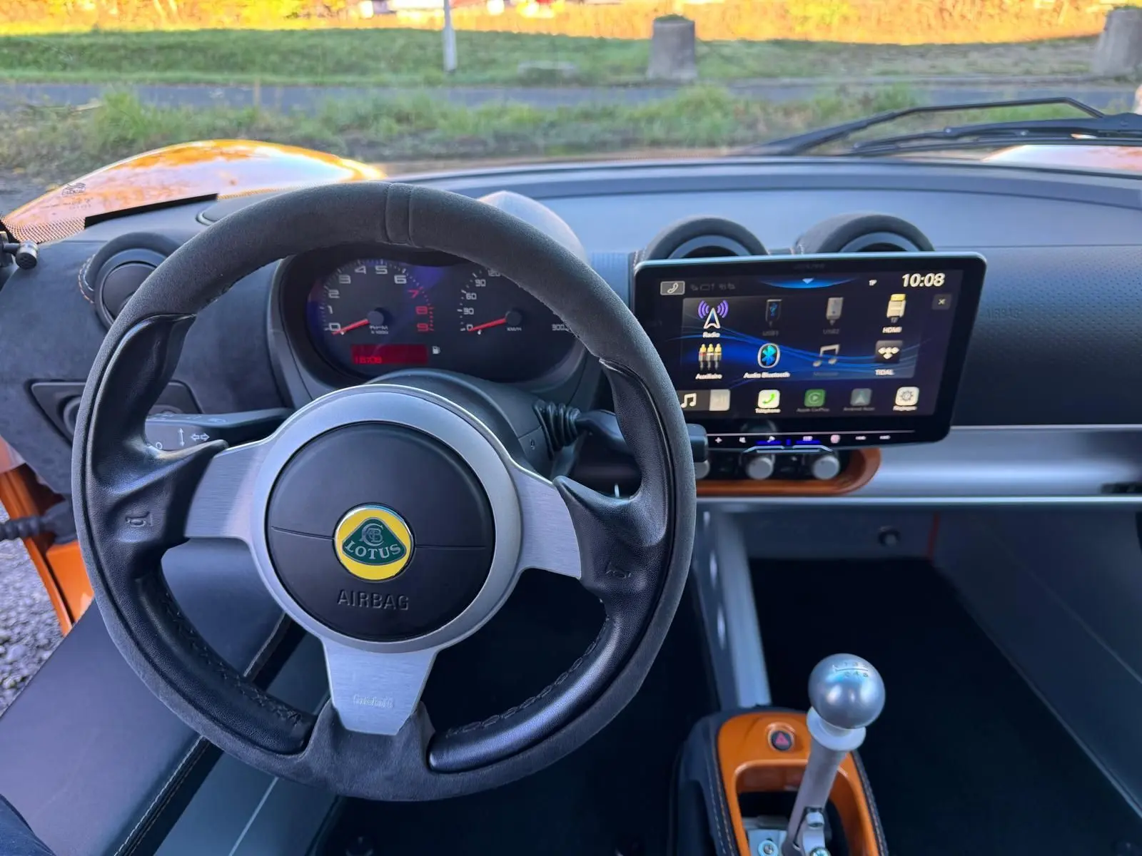 Vue intérieure centrée sur le volant cuir noir et le tableau de bord avec écran tactile de la Lotus Elise 3 Cup 250 orange.