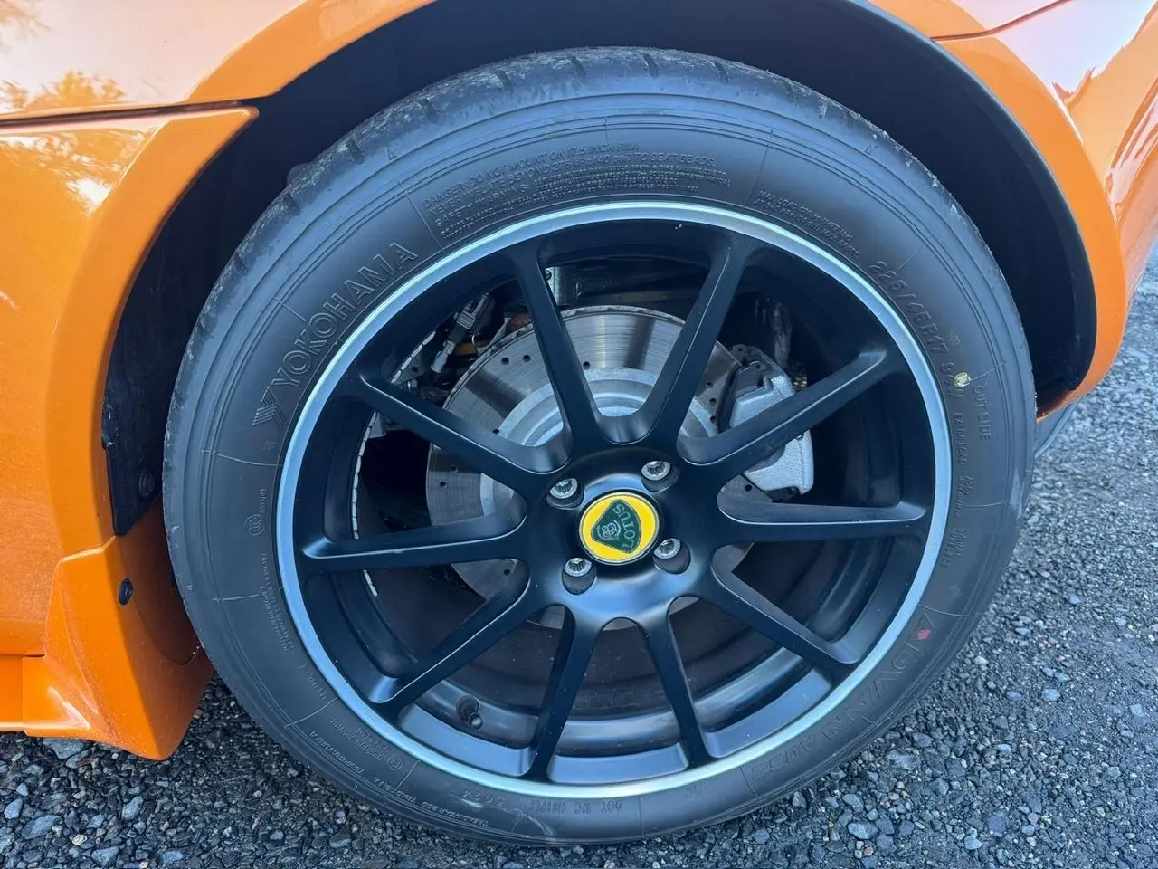 Gros plan sur la jante avant droite noire satinée de la Lotus Elise 3 Cup 250 orange, avec logo central jaune visible.