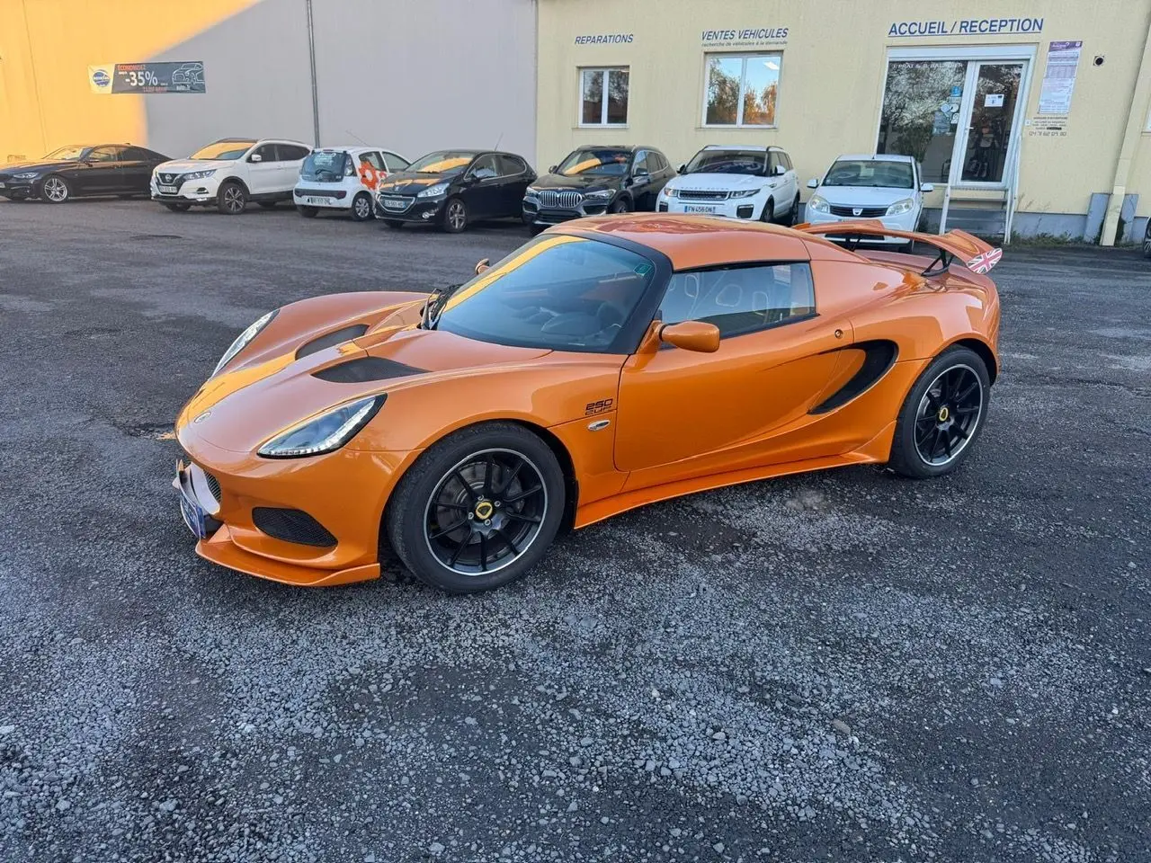 Lotus Elise 3 Cup 250 orange vue 3/4 avant droit avec jantes noires et aileron arrière marqué Union Jack.
