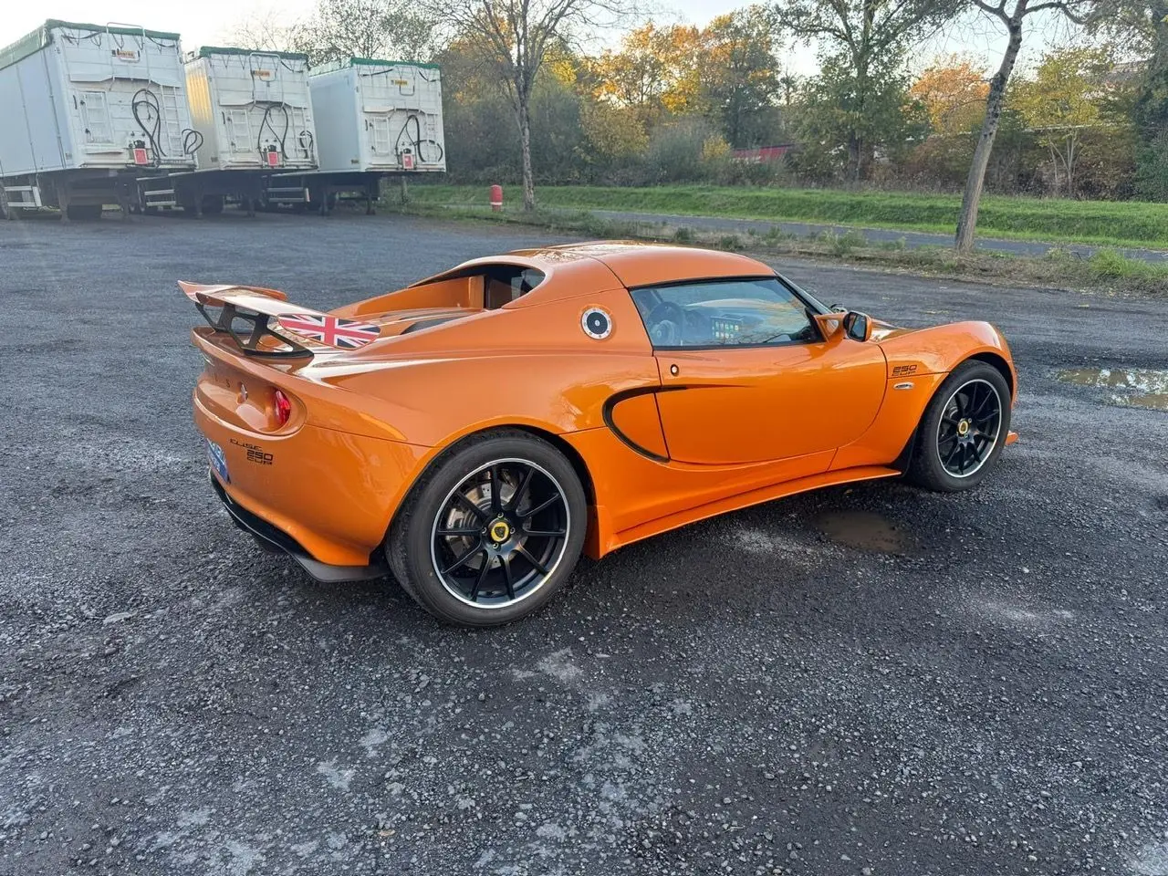Lotus Elise 3 Cup 250 orange vue 3/4 arrière droit, jantes noires satinées et aileron avec drapeau britannique.
