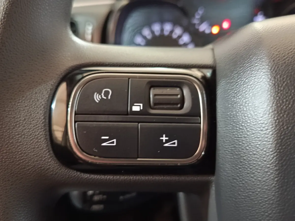 Gros plan sur les commandes noires du volant de la Citroën C3 blanche, avec boutons de volume et reconnaissance vocale.