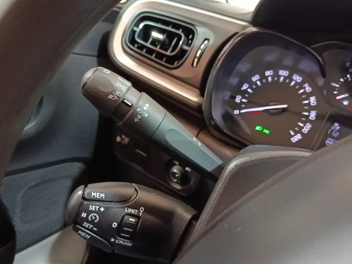 Gros plan sur le tableau de bord et commandes au volant de la Citroën C3 blanche, affichage vitesse et régulateur visible.