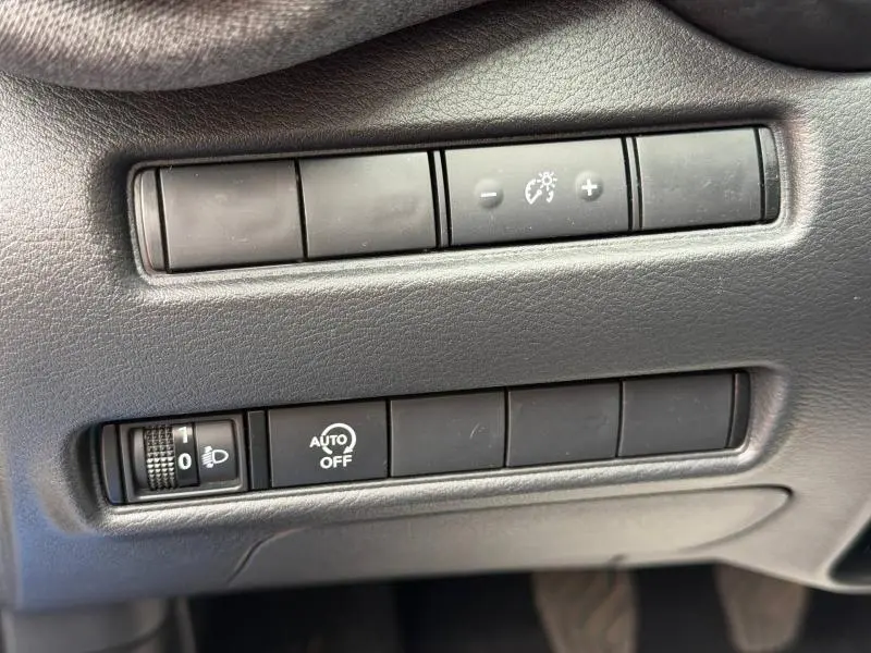 Gros plan sur les commandes noires du tableau de bord du Nissan Juke 2025, réglage éclairage et fonction auto off visibles.